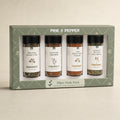 A boxed spice gift set labeled PINE & PEPPER, containing four glass spice bottles with black caps and white labels, displayed in a sage green presentation box on a light neutral background.