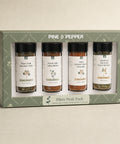 A boxed spice gift set labeled PINE & PEPPER, containing four glass spice bottles with black caps and white labels, displayed in a sage green presentation box on a light neutral background.